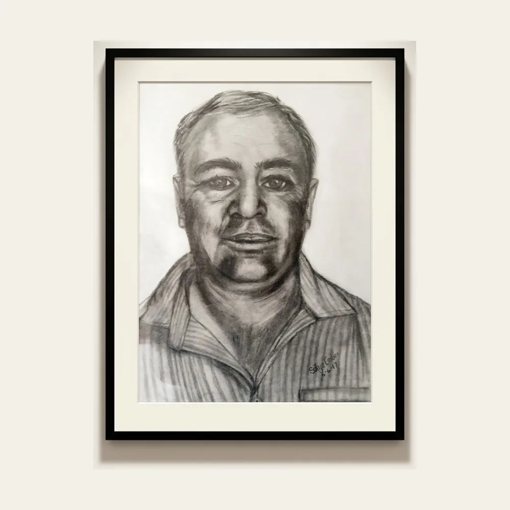 Portrait of a Man — a charcoal head-and-shoulders portrait of a man in a striped collared shirt, mounted in a black frame.