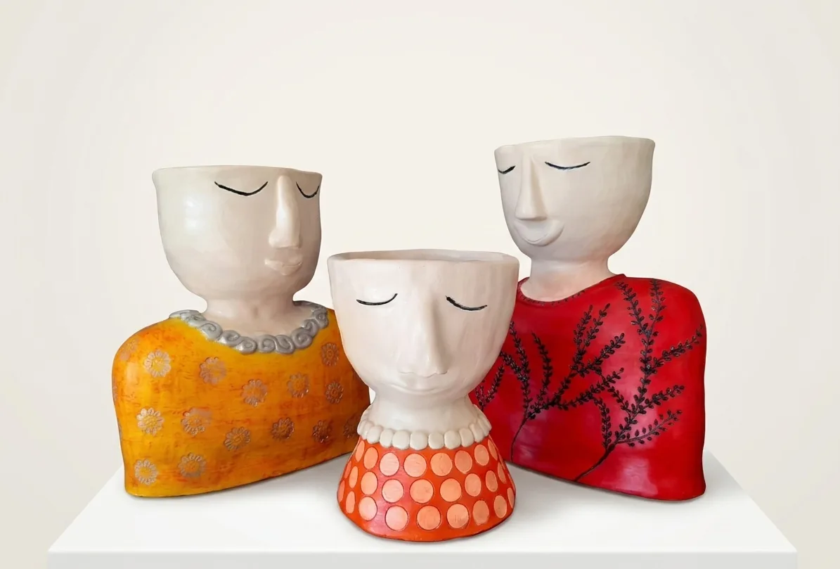 Three Graces — a set of three ceramic bust vessels with closed eyes, glazed in saffron, coral and red.